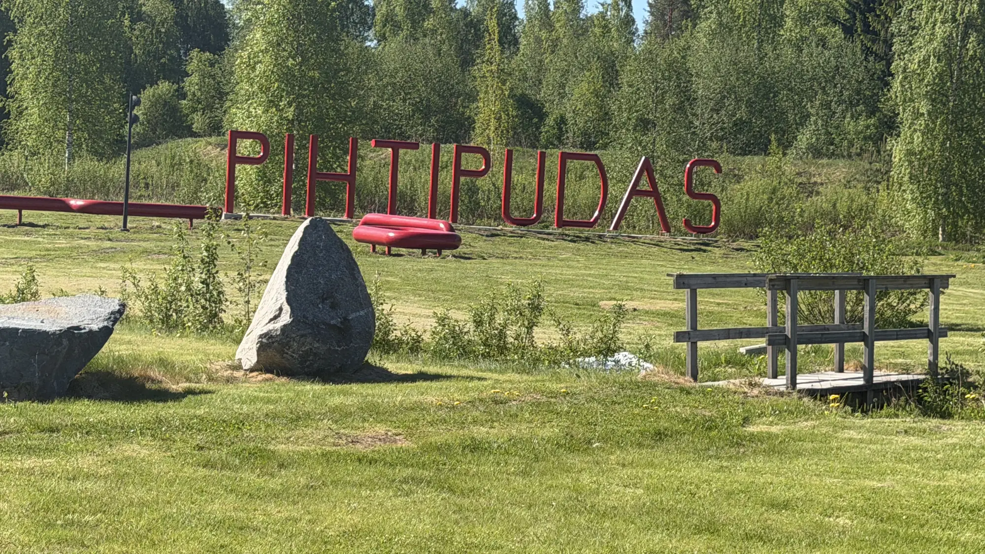 Punaiset PIHTIPUDAS-kirjaimet puiston nurmella